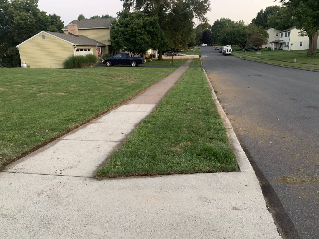 A street with a sidewalk and grass in front of a house.